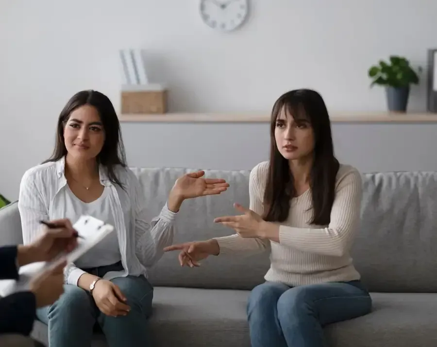 Una persona escribe en un portapapeles, con una pareja borrosa en el fondo en un sofá.