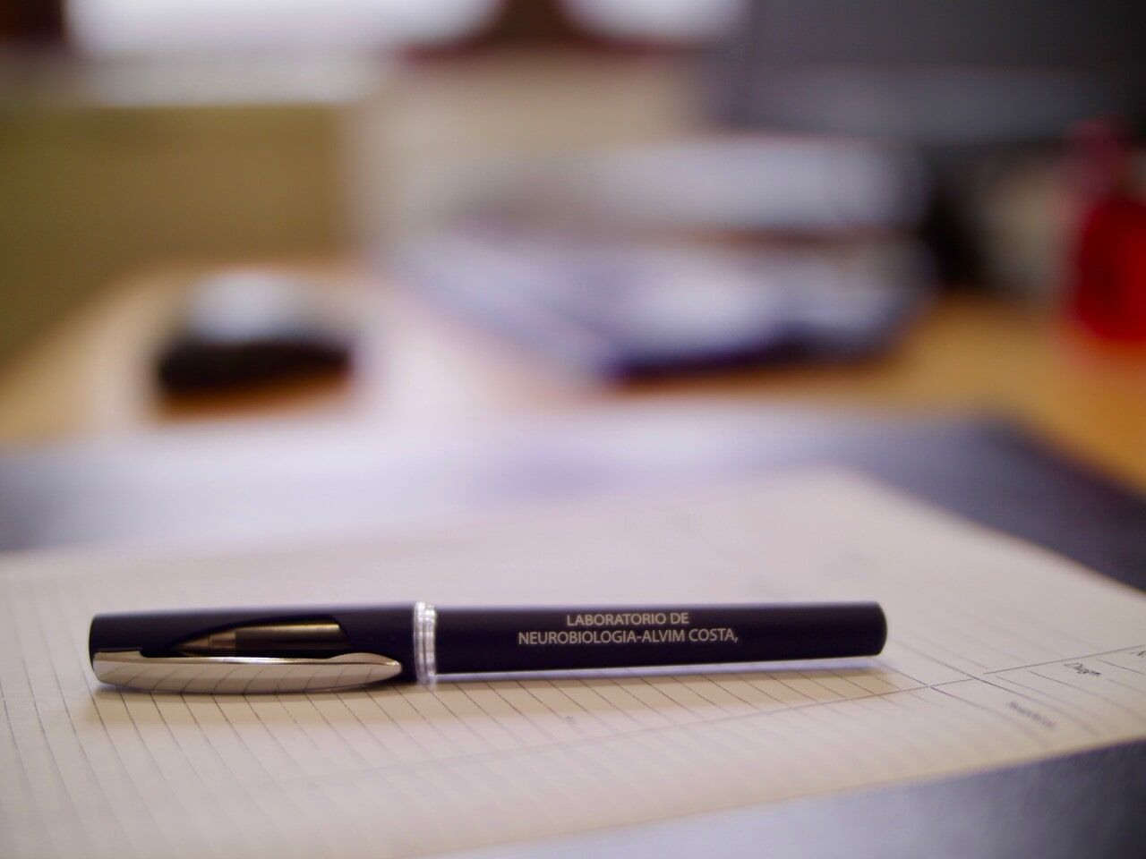 Uma caneta azul escura com detalhes prateados sobre uma superfície coberta de papel. O fundo está desfocado.