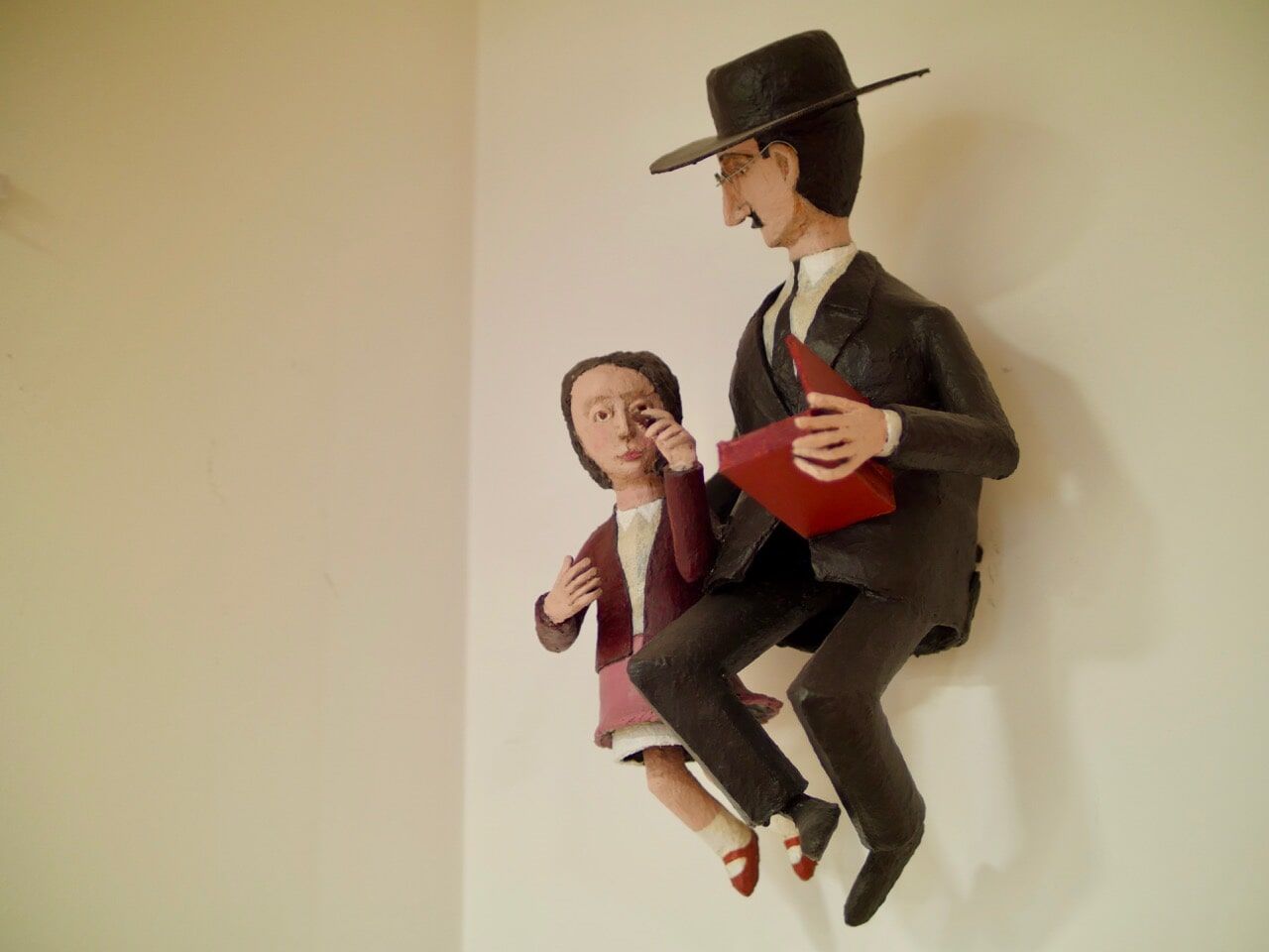 Escultura de um homem de terno e chapéu, segurando um livro, com uma criança ao lado.