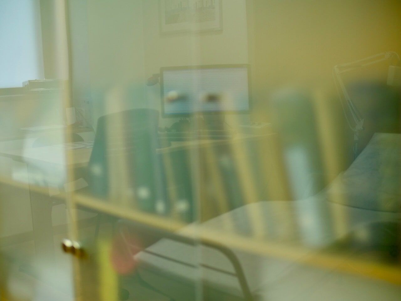 Estantes de livros atrás de vidro, livros verdes, prateleiras douradas, ligeiramente desfocadas.