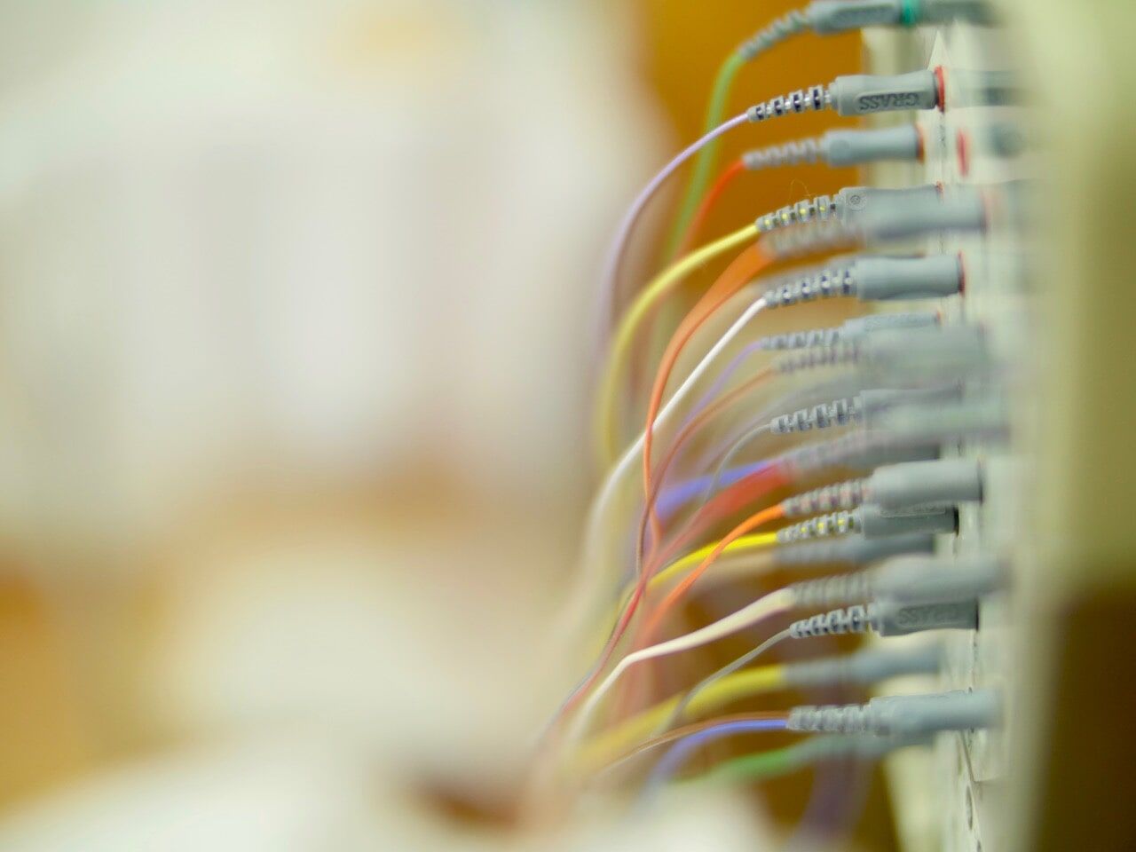 Imagem em close-up de um dispositivo médico com fios coloridos conectados, fundo desfocado.
