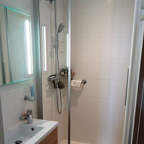 A bathroom with a sink , shower and mirror.