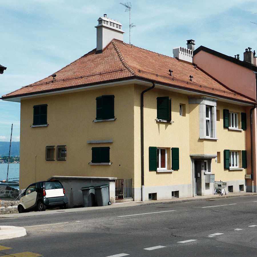 A yellow building with a brown roof and green shutters