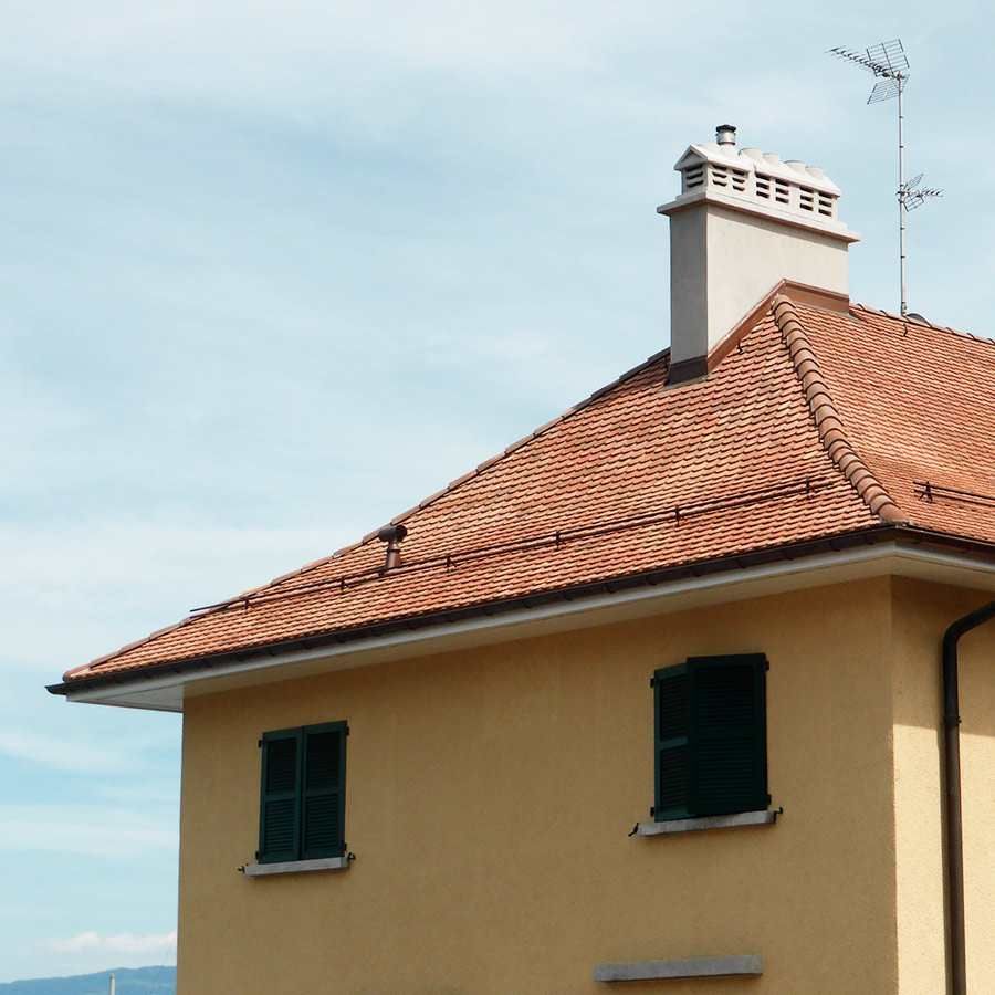 A yellow house with a tiled roof and a chimney on top
