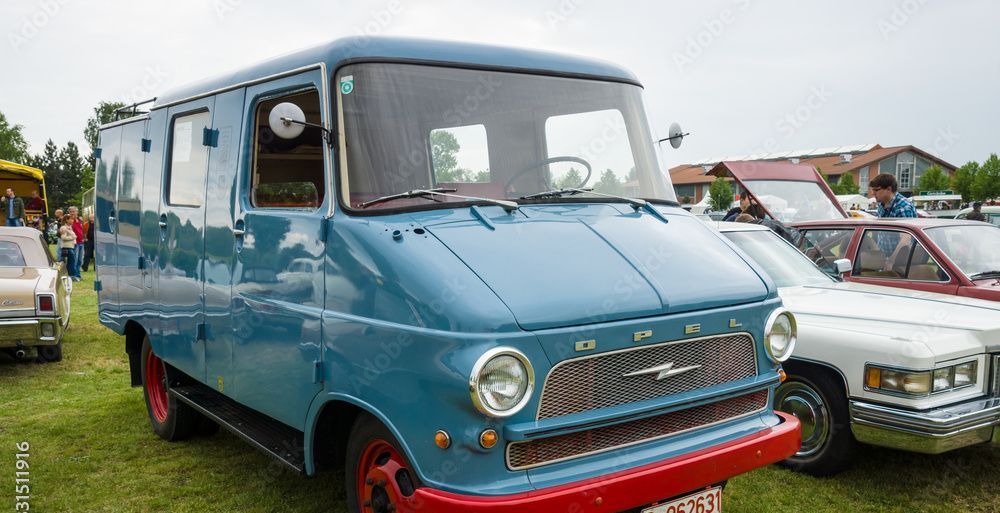 Ein blauer Lieferwagen mit roter Stossstange steht neben einem weissen Auto.