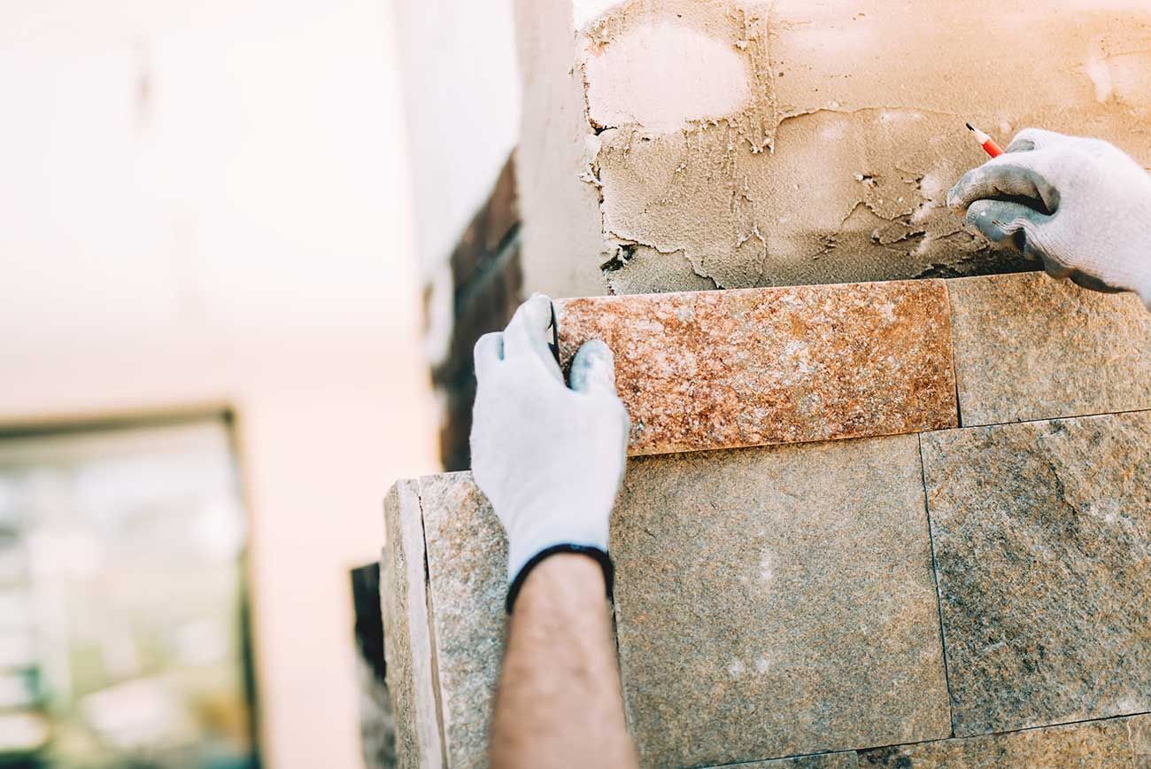 Manos colocando mortero en una pared de ladrillos durante la construcción.