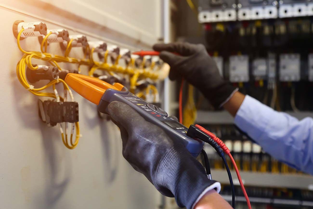 Técnico con guantes probando cables en un panel eléctrico con un multímetro.