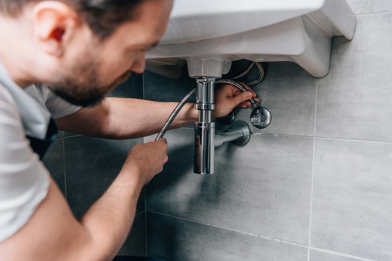 Un fontanero aprieta con una llave inglesa la tubería del fregadero debajo del lavabo del baño.