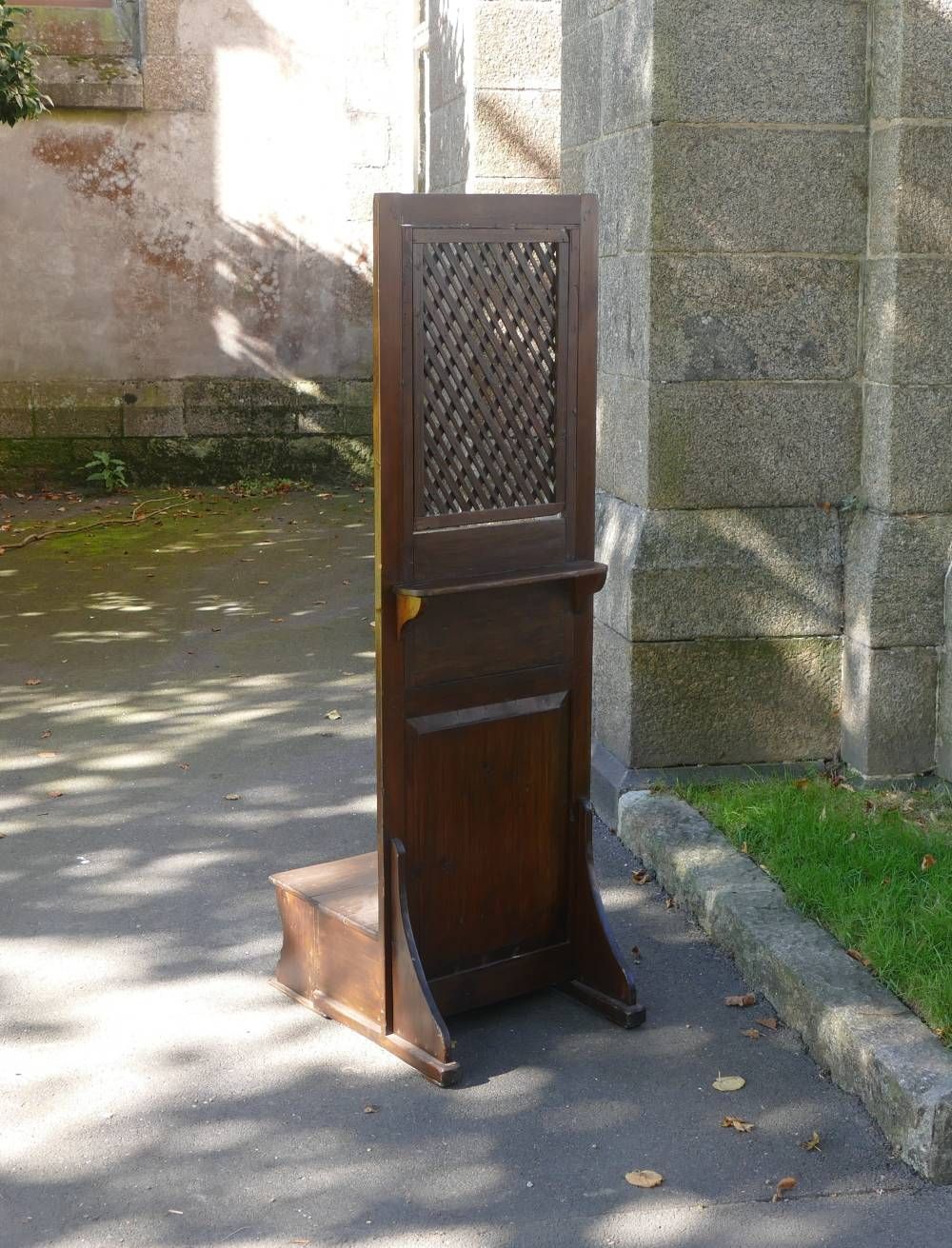 Pupitre ou lutrin d’extérieur en bois, avec un plateau à treillis, sur un chemin de pierre ensoleillé, près d’un mur