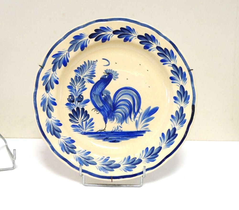 Assiette bleue et blanche ornée d’un coq et d’une bordure florale, sur un présentoir