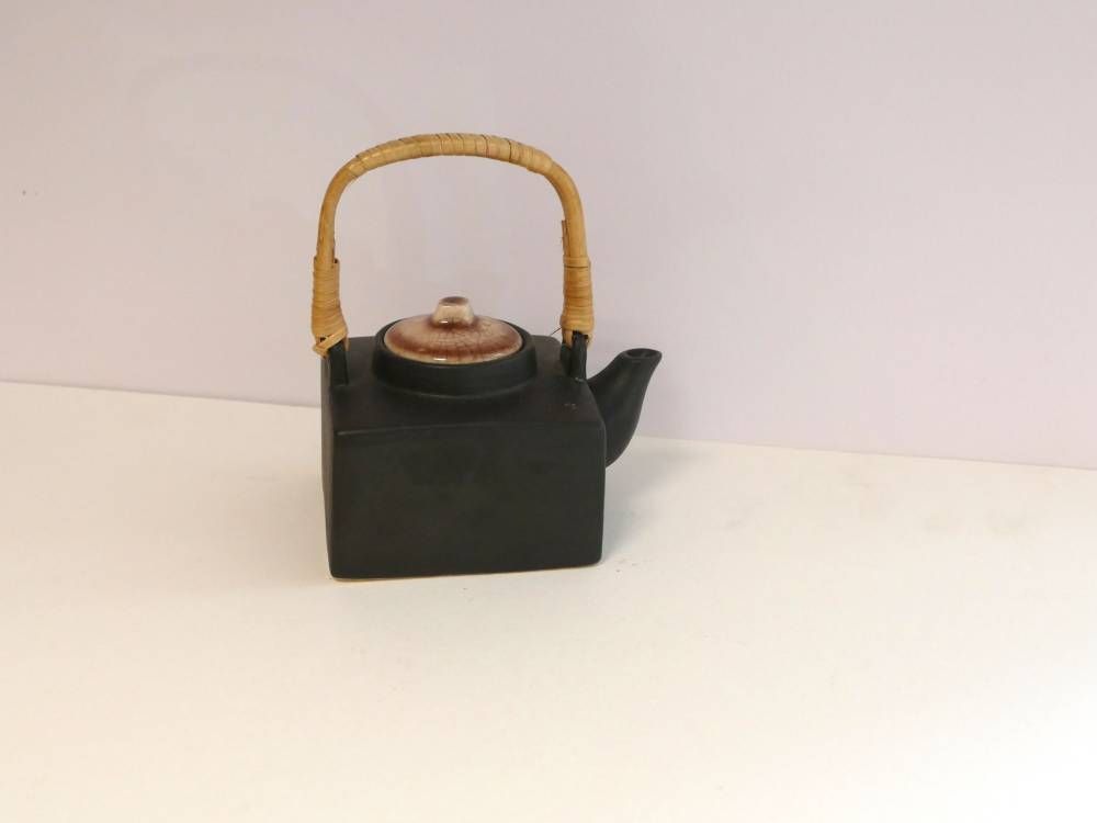 Petite théière noire avec une anse tressée sur une surface blanche