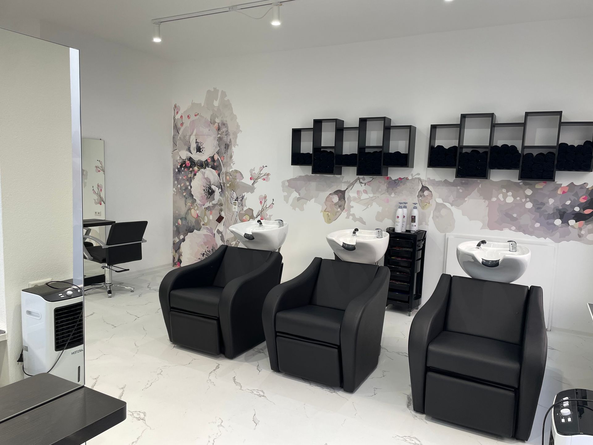 Ein Friseursalon mit drei schwarzen Stühlen und Waschbecken.