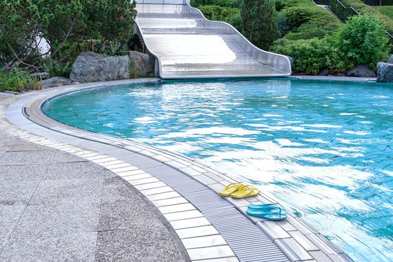 Geschwungener Aussenpool mit türkisfarbenem Wasser, Steinterrasse und einem gelben Handtuch am Rand