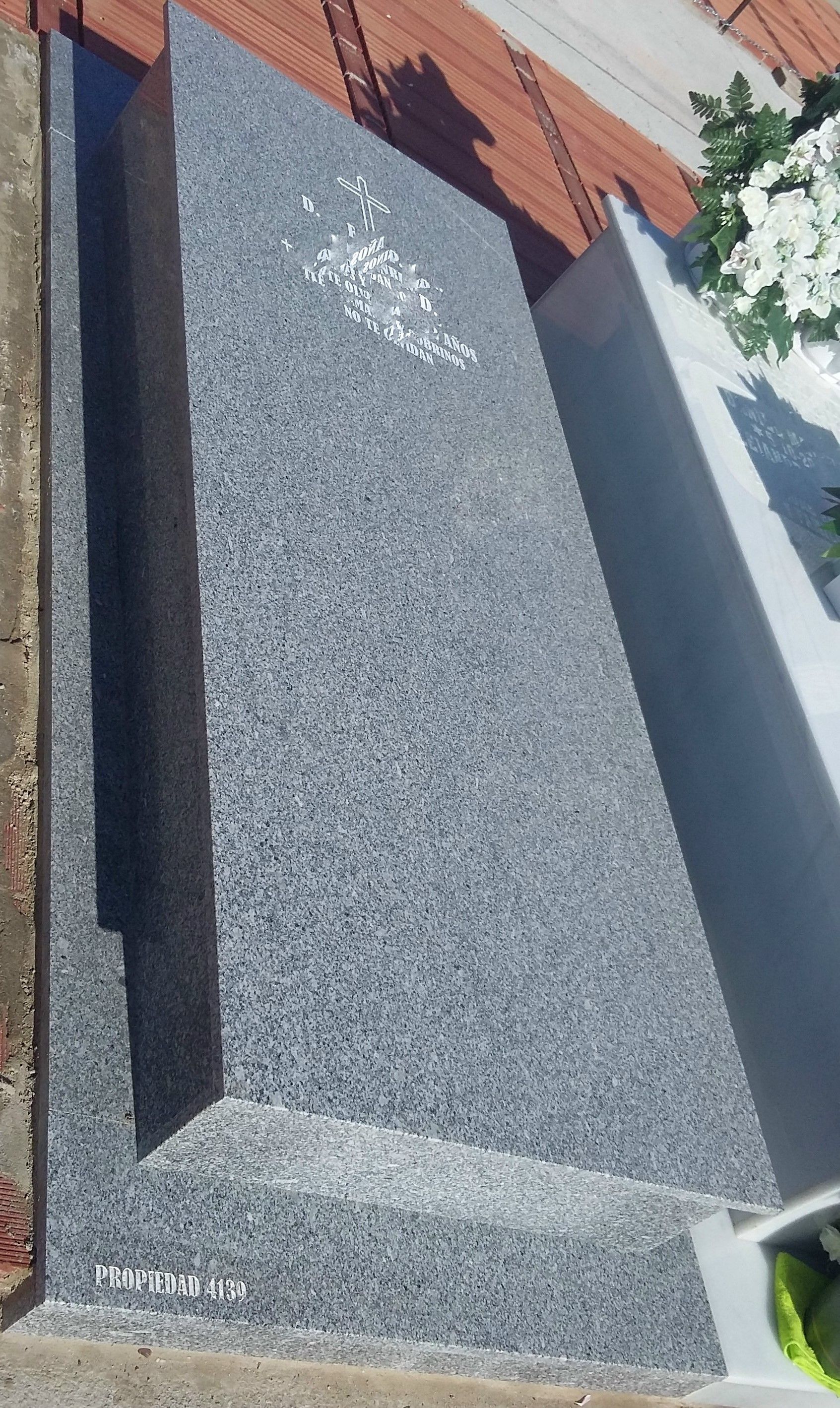 Una lápida con una sombra sobre ella se encuentra al lado de una pared de ladrillos.