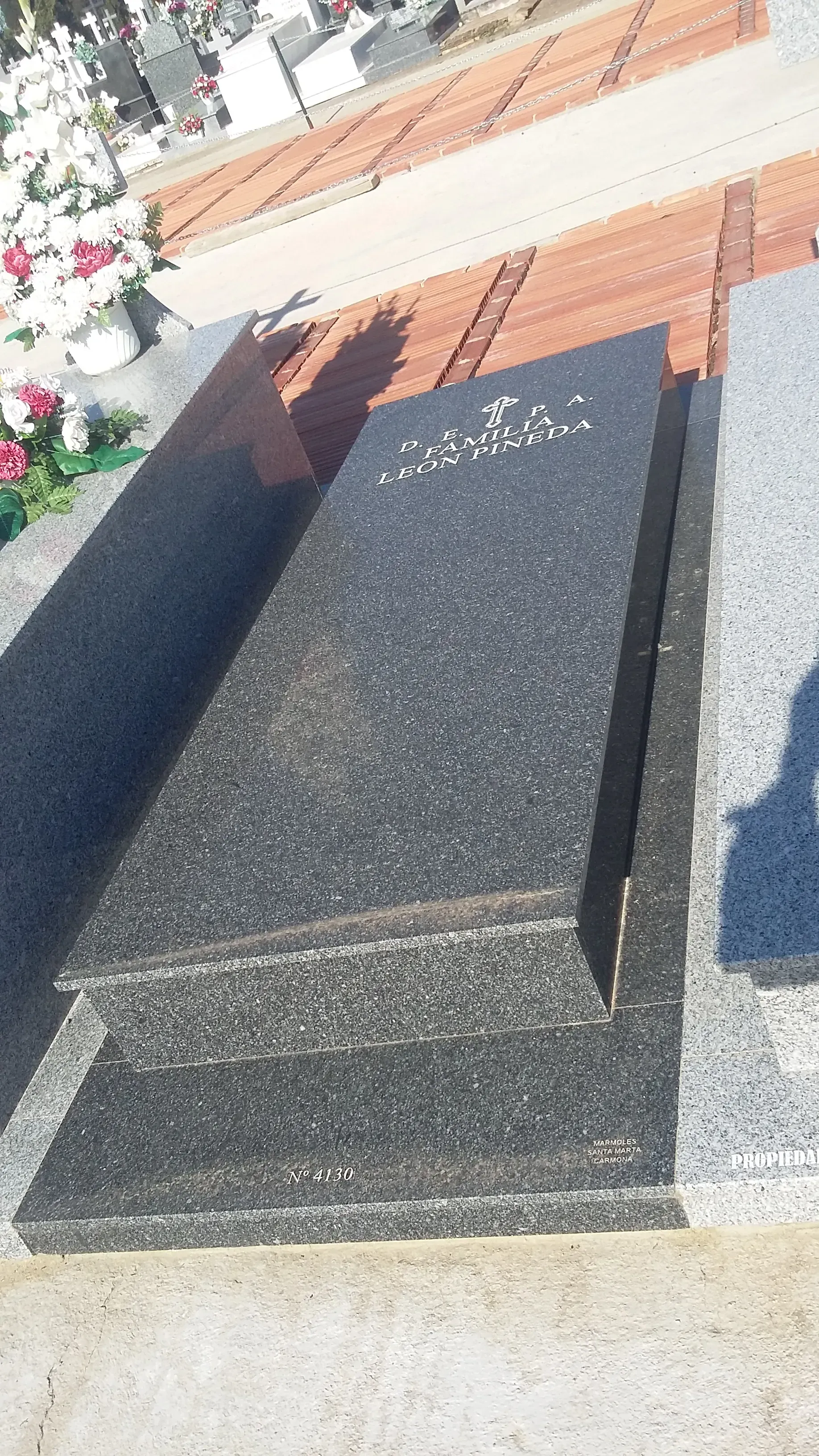 Una lápida negra en un cementerio con flores en el fondo.