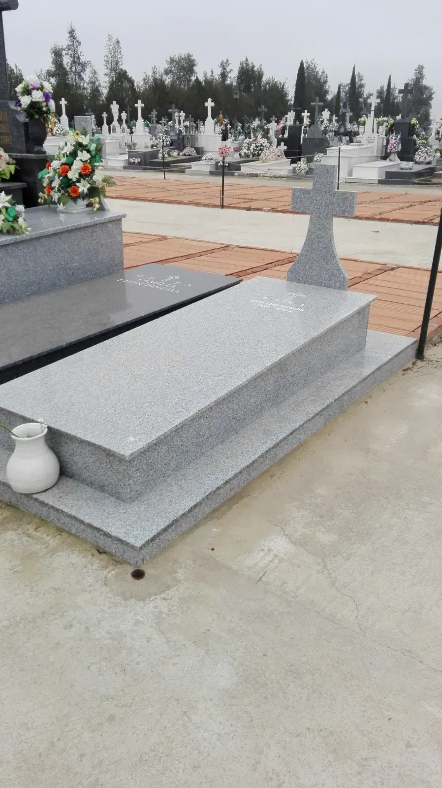 Una tumba en un cementerio con flores y una cruz.