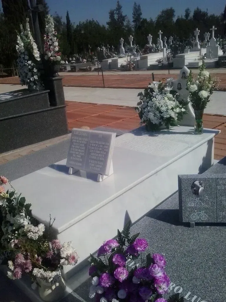 Una tumba en un cementerio con flores moradas y blancas.
