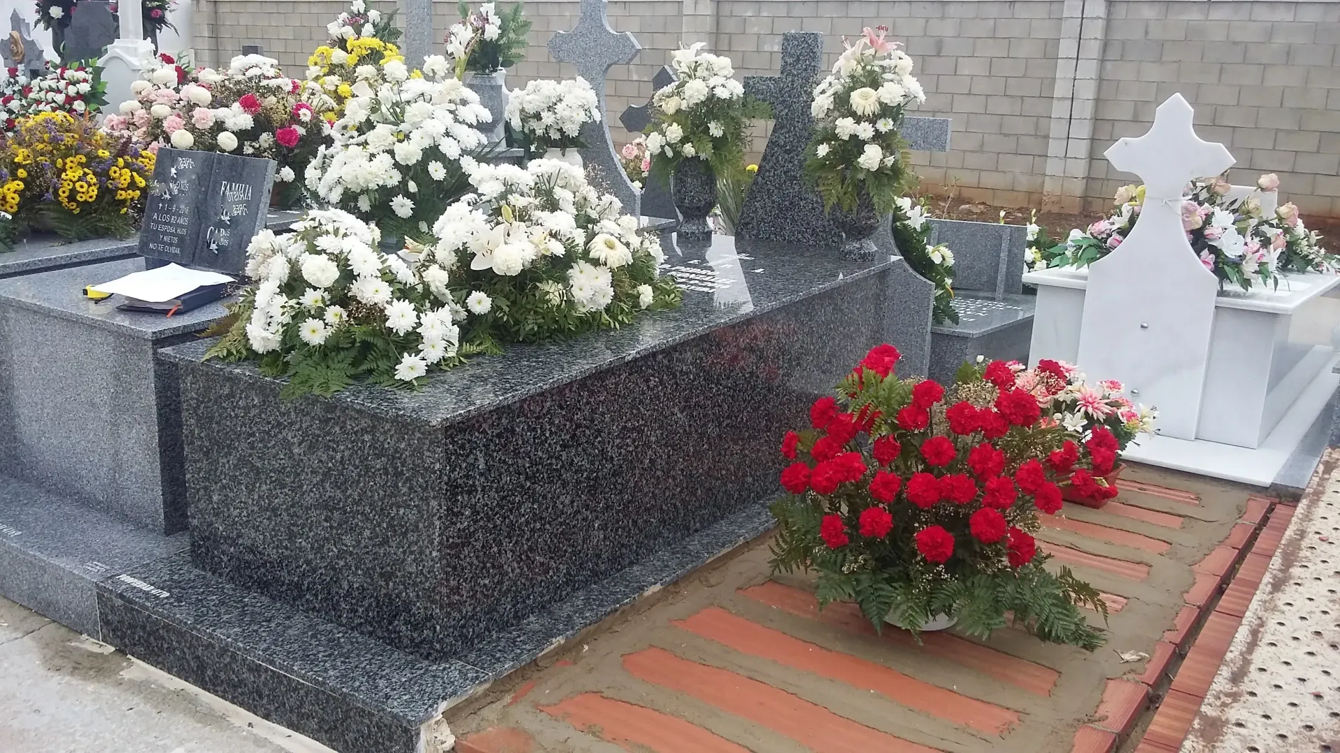 Un cementerio con flores en las tumbas y un ramo de rosas rojas en el suelo.