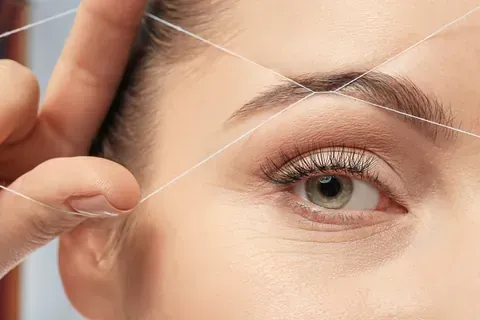 Una mujer se depila las cejas con un hilo.