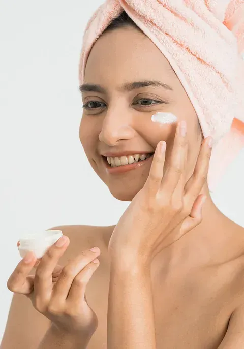 Una mujer con una toalla envuelta alrededor de su cabeza se aplica una crema en la cara.