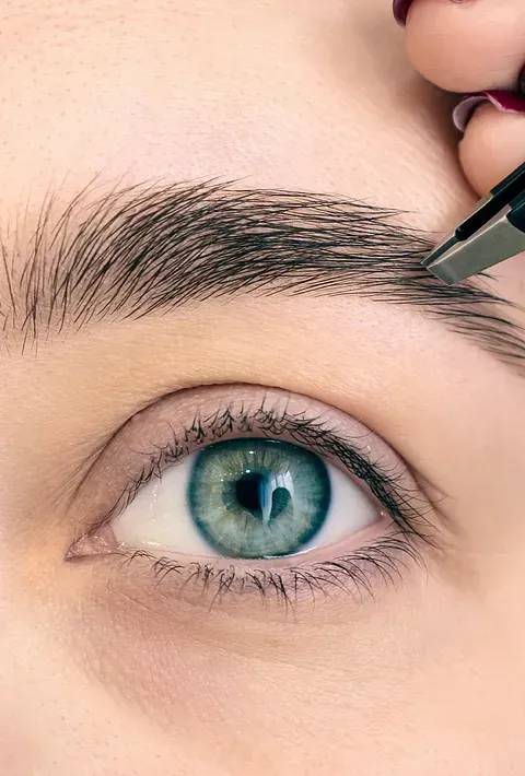 Una mujer se está recortando las cejas con pinzas.