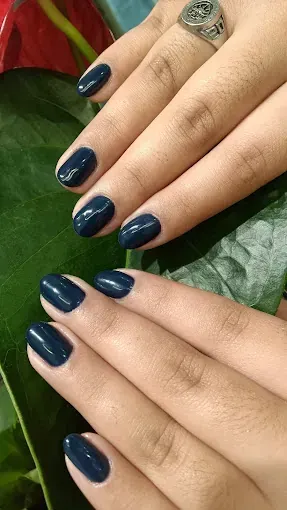 Un primer plano de las uñas de una persona con esmalte azul y un anillo.