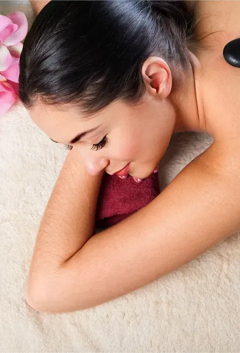 Una mujer está acostada en una cama recibiendo un masaje con piedras calientes.