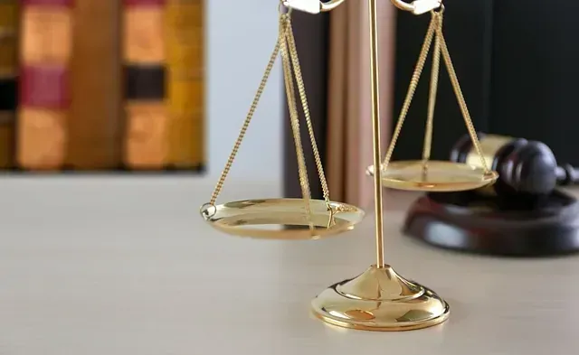 Balanza dorada de la justicia con un mazo y libros al fondo, sobre una mesa.