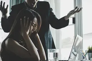 Un hombre le grita a una mujer que se tapa los oídos en un escritorio.