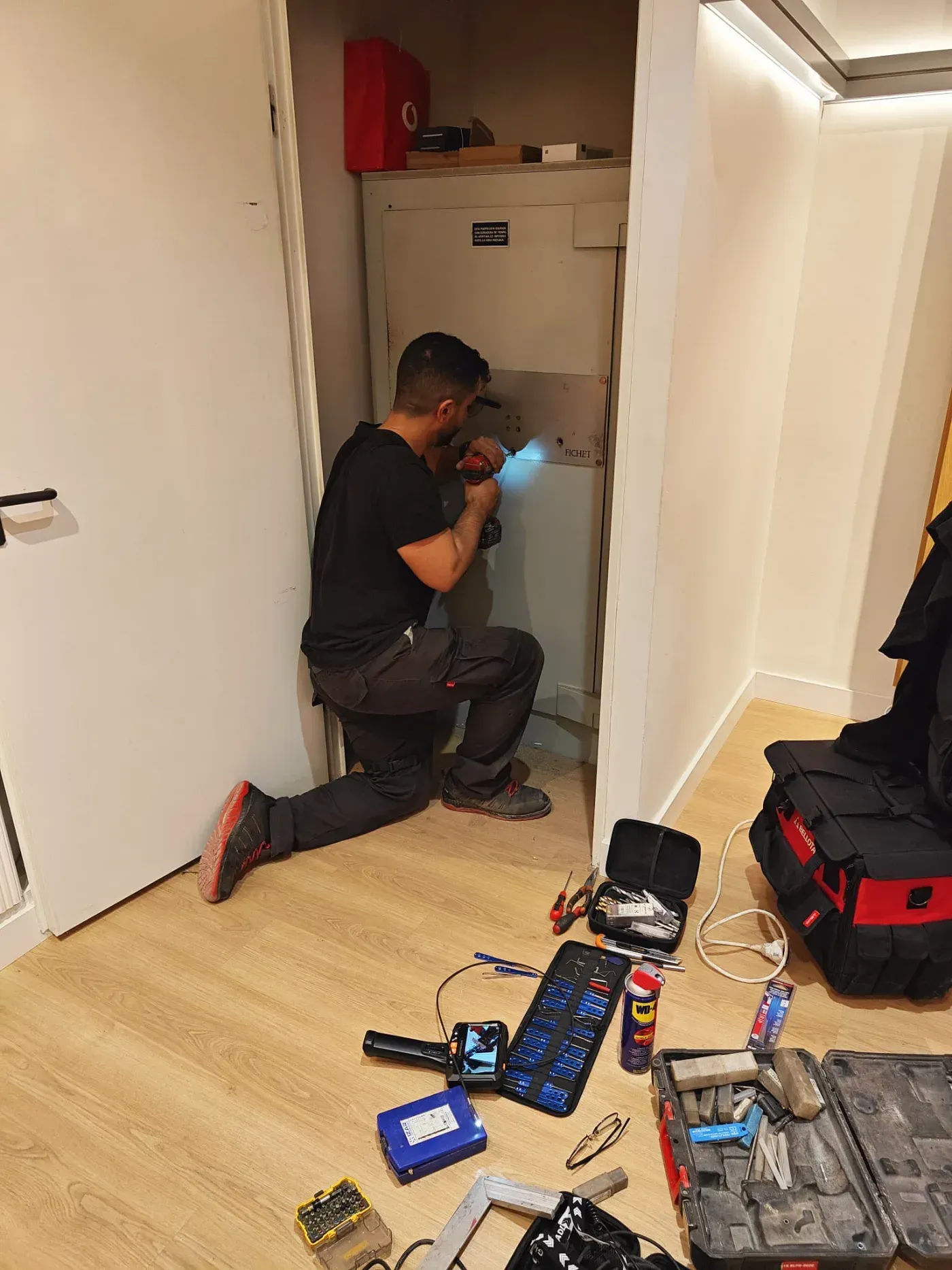 Hombre arrodillado, usando una linterna y un taladro