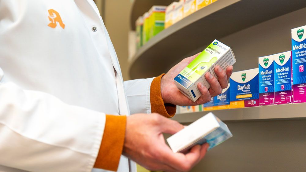 Ein Apotheker hält in einer Apotheke eine Schachtel mit Medikamenten in den Händen.