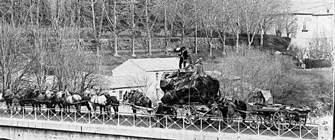 Photographie noir et blanc d'un chariot plein à craquer tiré par 6 chevaux de trait sur un pont en 1902