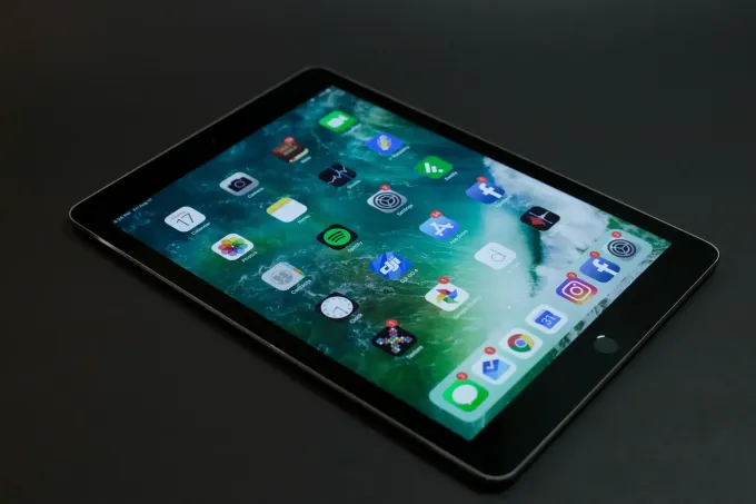 IPad negro que muestra íconos de aplicaciones en una superficie oscura.