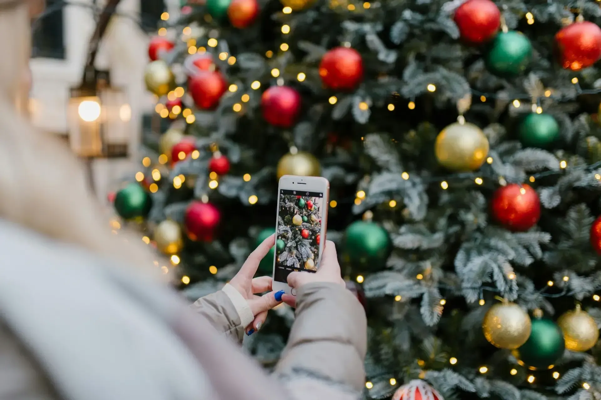 Persona tomando fotografía de árbol de Navidad con adornos y luces.