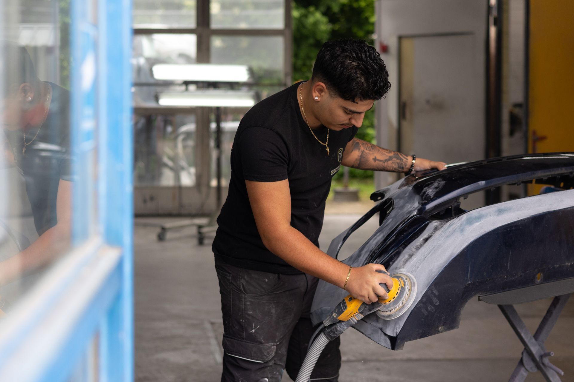 Ein Mann schleift in einer Garage eine Autostoßstange ab.