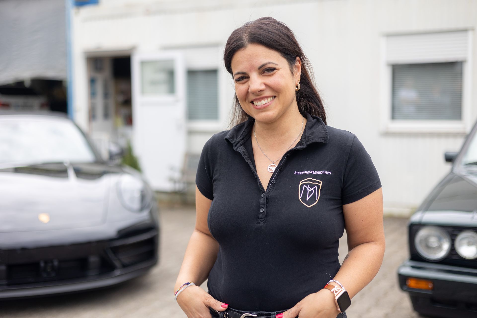 Eine Frau in einem schwarzen Hemd steht vor zwei Autos.