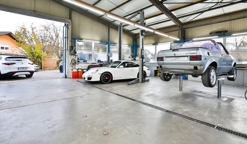 Zwei Autos stehen auf einer Hebebühne in einer Garage.