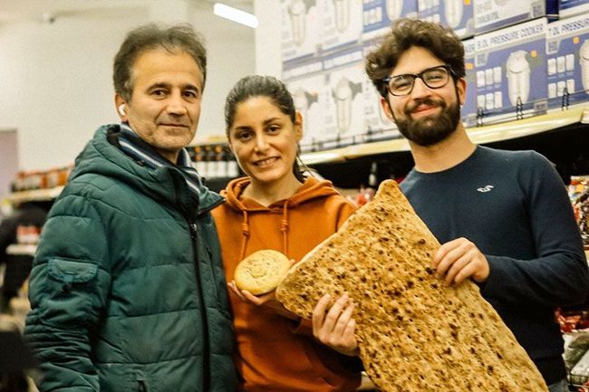 Eine Gruppe von Menschen steht in einem Laden nebeneinander und hält ein großes Stück Brot in den Händen.