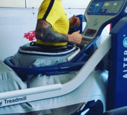 Persona con maglietta gialla che si allena su un tapis roulant AlterG. La macchina ha una camera d'aria gonfia intorno alla vita e dettagli blu.