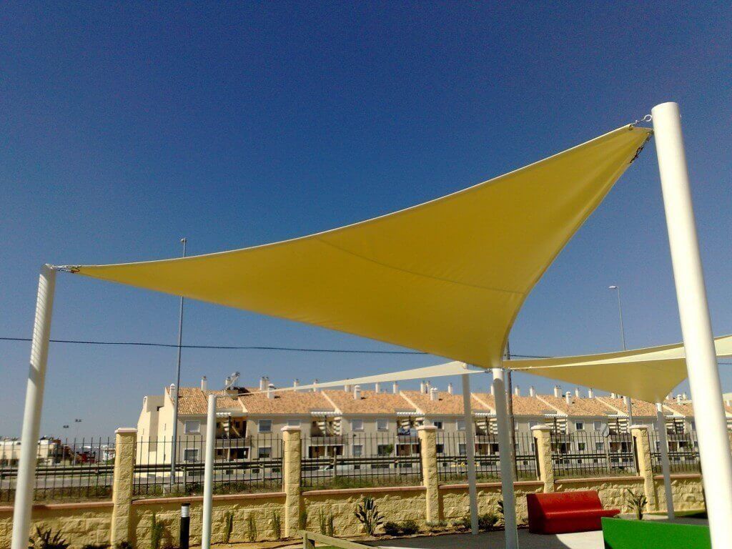 Una sombrilla amarilla en forma de triángulo con un sofá rojo debajo.