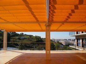 Un gran toldo naranja cubre un balcón con vistas a una ciudad.