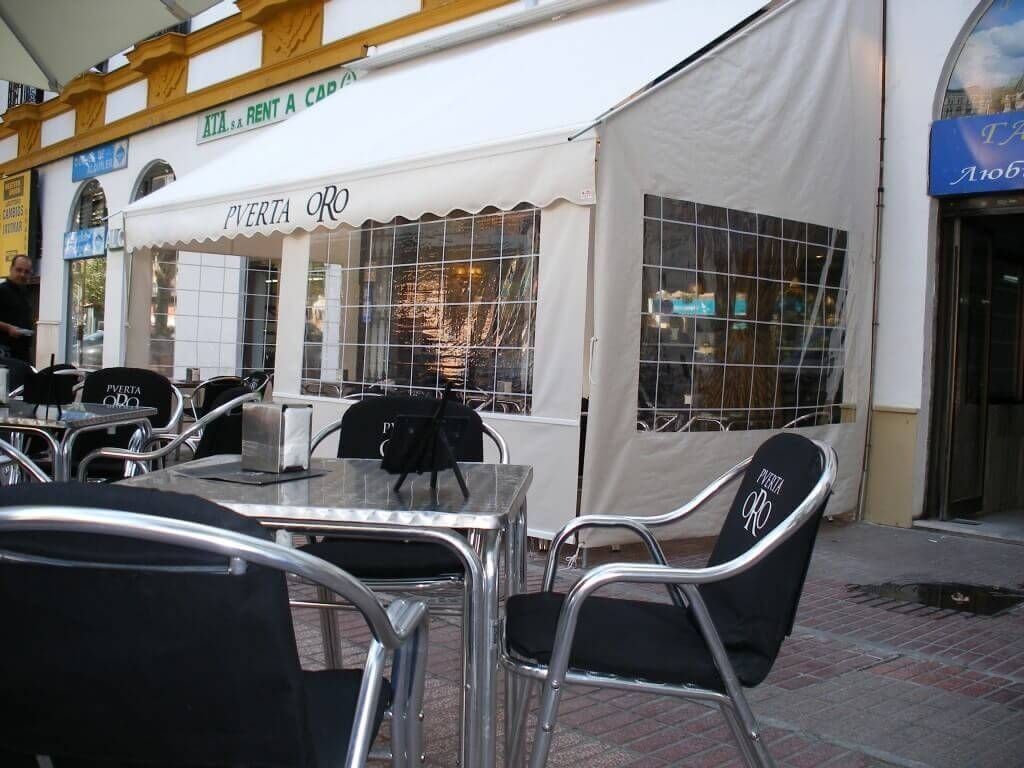 Mesas y sillas en el exterior de un restaurante con un toldo blanco.