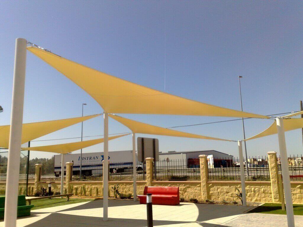 Un parque con una sombrilla amarilla y un banco rojo.