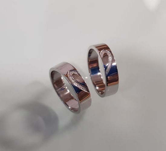 Un par de anillos de boda con un diseño de corazón están sobre una superficie blanca.
