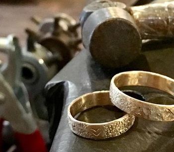 Dos anillos de oro están sobre una mesa al lado de un martillo.