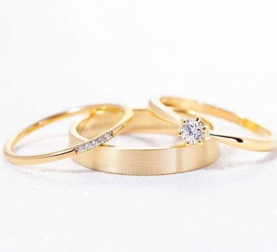 Tres anillos de oro se apilan uno encima del otro sobre una superficie blanca.