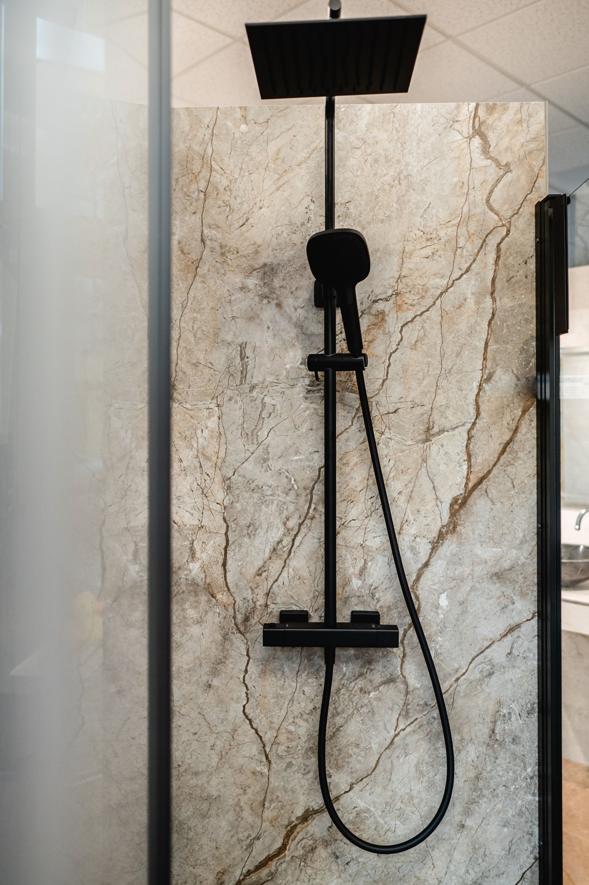 Schwarzer Duschkopf und Handbrause vor einer Wand in Marmoroptik in einem modernen Badezimmer.