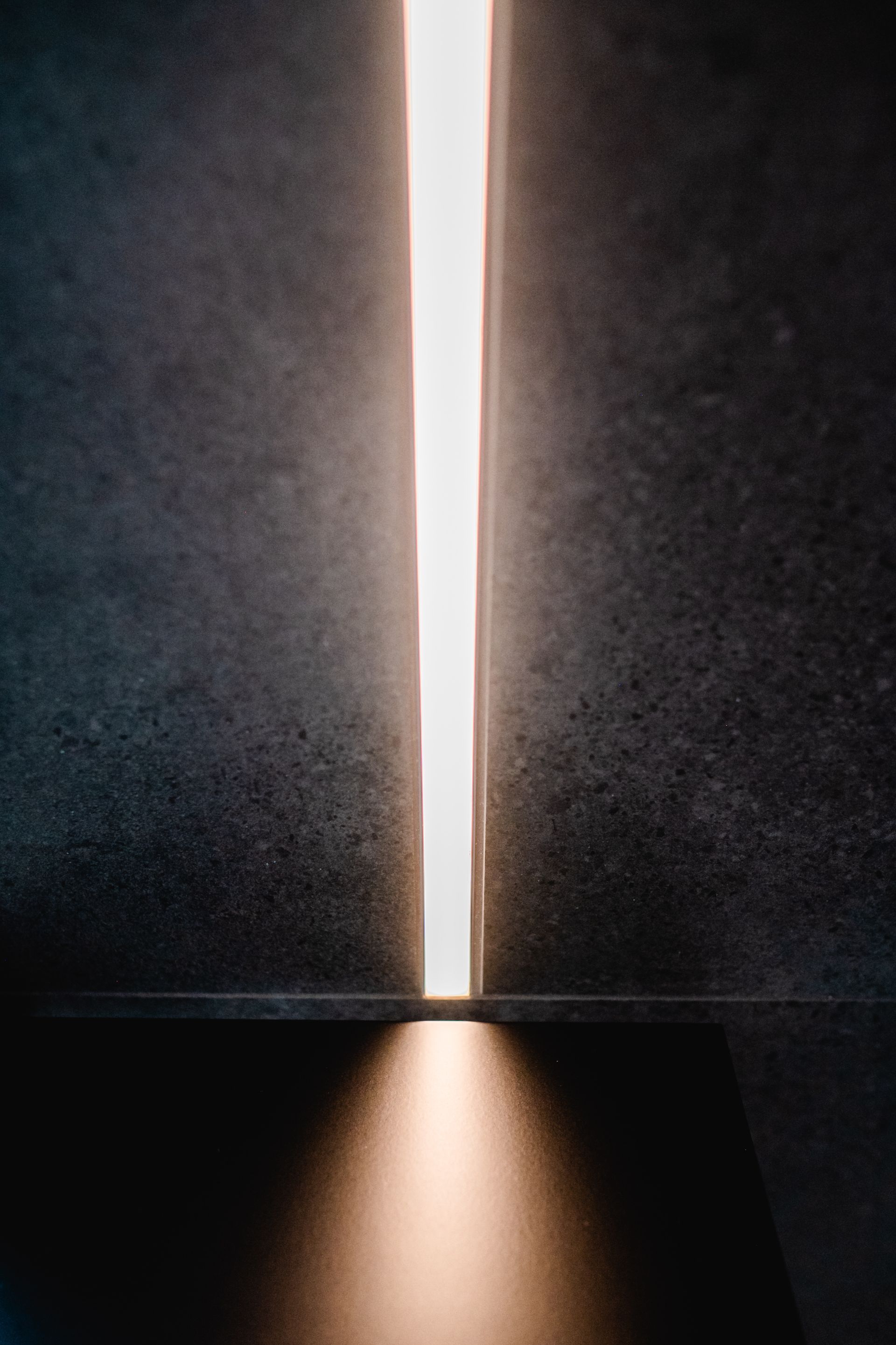 Eine helle Lichtlinie schneidet vertikal eine dunkle, strukturierte Oberfläche. Unten leuchtet ein Strahl.