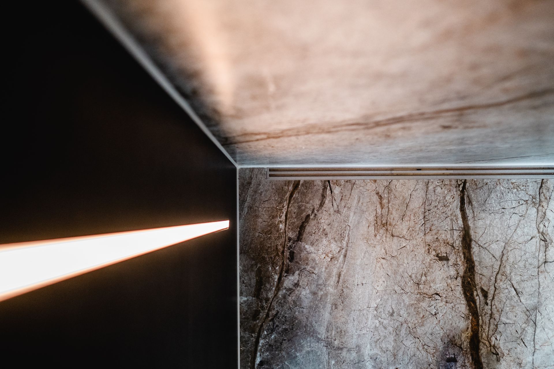 Licht strömt durch einen Schlitz und beleuchtet eine strukturierte Steinwand und eine Betondecke.