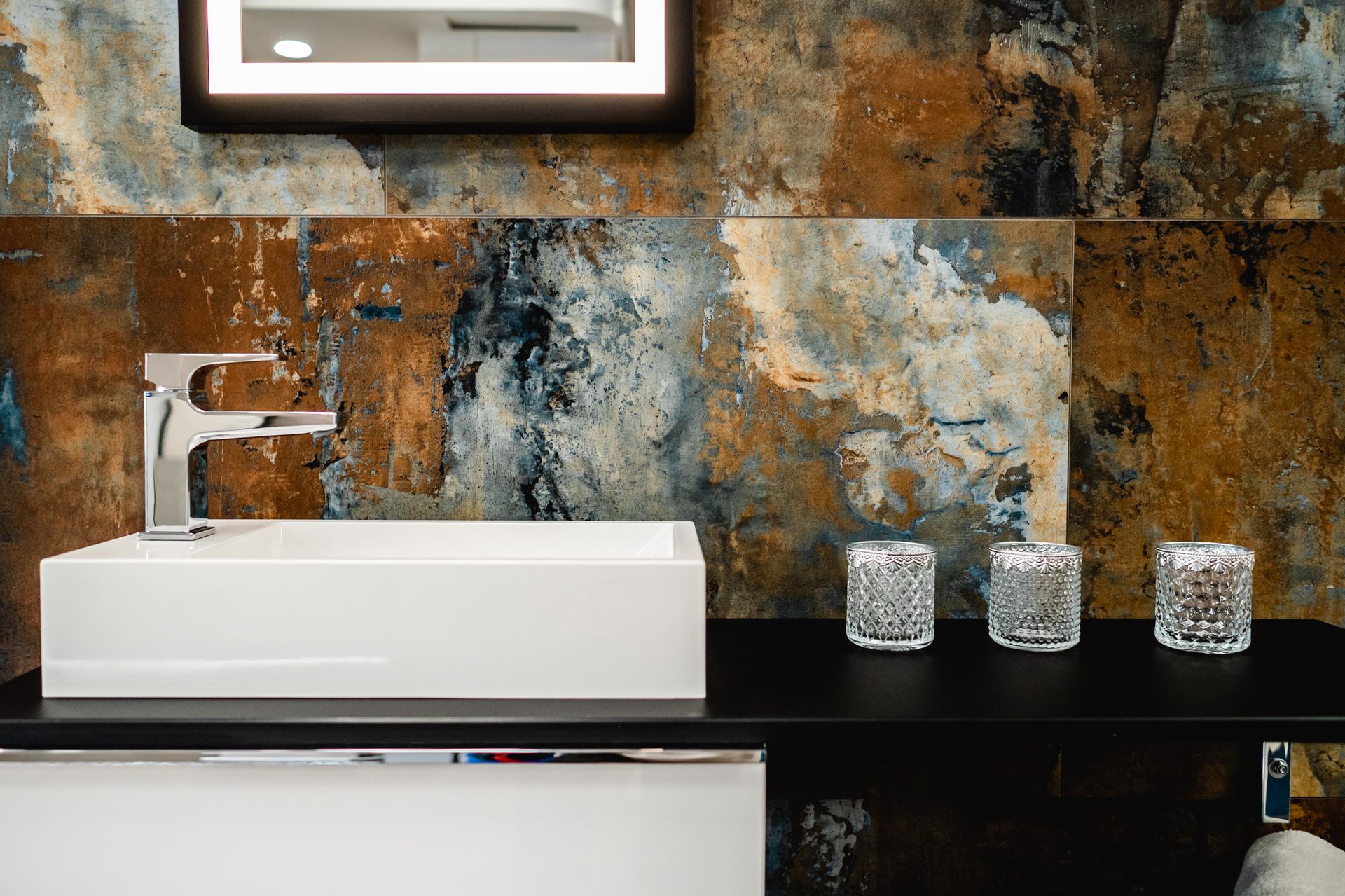 Badezimmer mit rechteckigem Waschbecken, Chromhahn, rustikalen Wandfliesen und Kerzen.